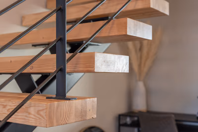 Close view of timber stair treads on a black steel post and rod railing, with a dried pampas arrangement in a vase in the background.